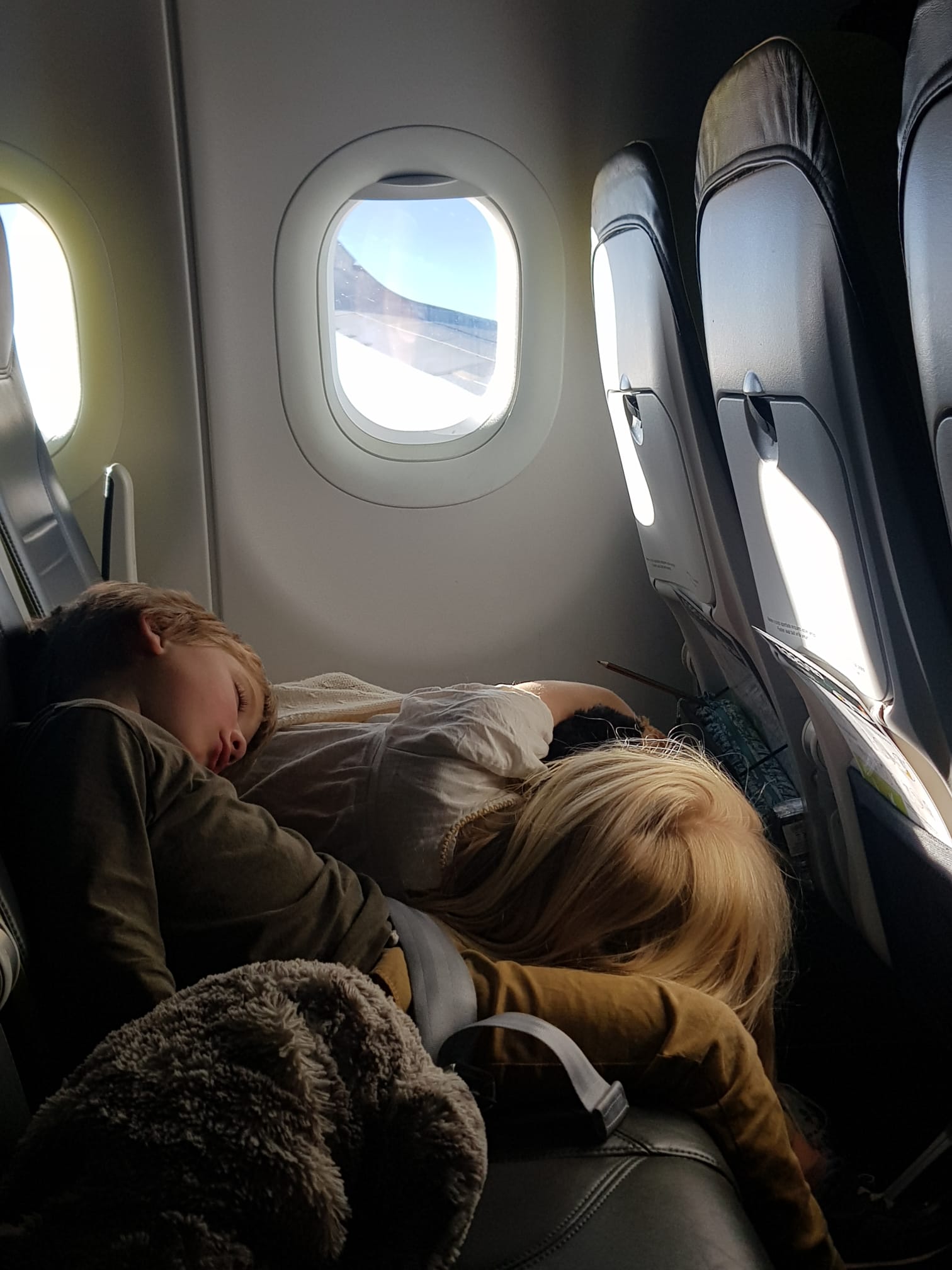Two children fast asleep on the flight home, teddy bear in tow