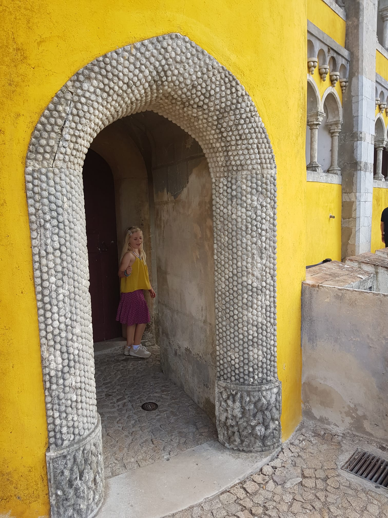 A young girl standing in wonder beneath a golden archway at Pena Palace, Sintra
